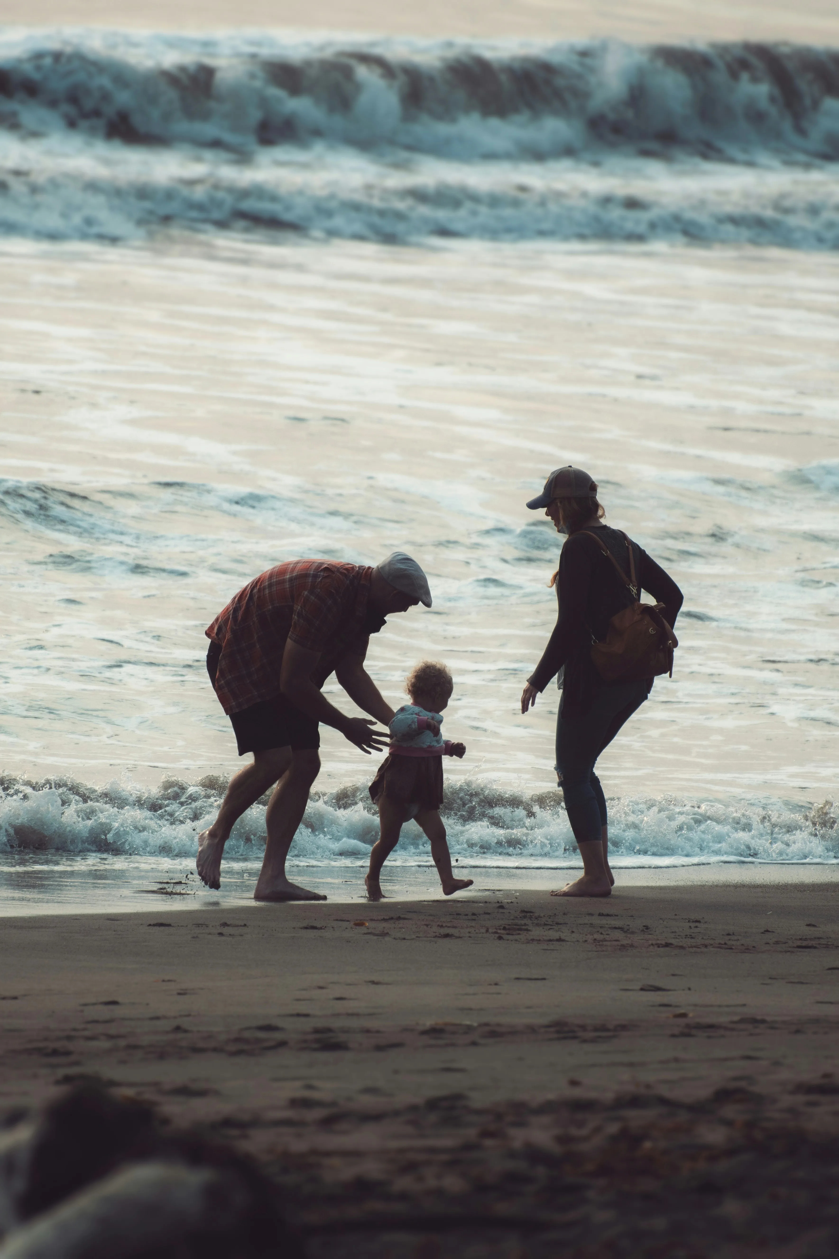 A mum, dad and toddler playing at the water's edge at dusk